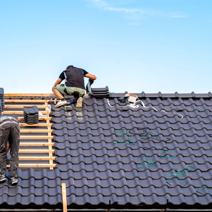 Two roofing professional laying and installing the tiles of a roof.